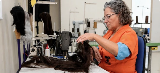 Trabajadora confeccionando una peluca con cabello donado en el taller