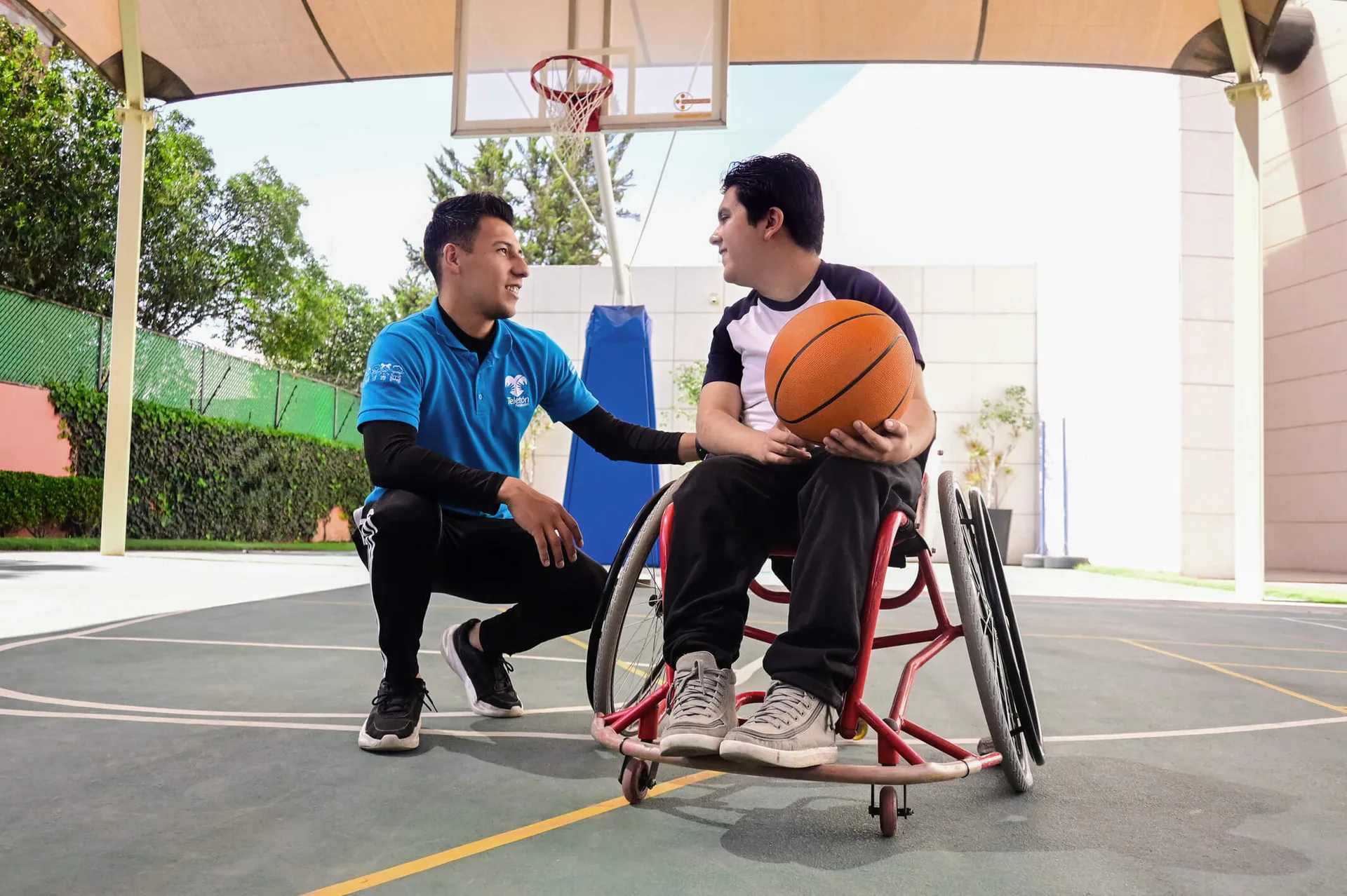 Voluntario jugando basquetbol en silla de ruedas con un niño en el CRIT