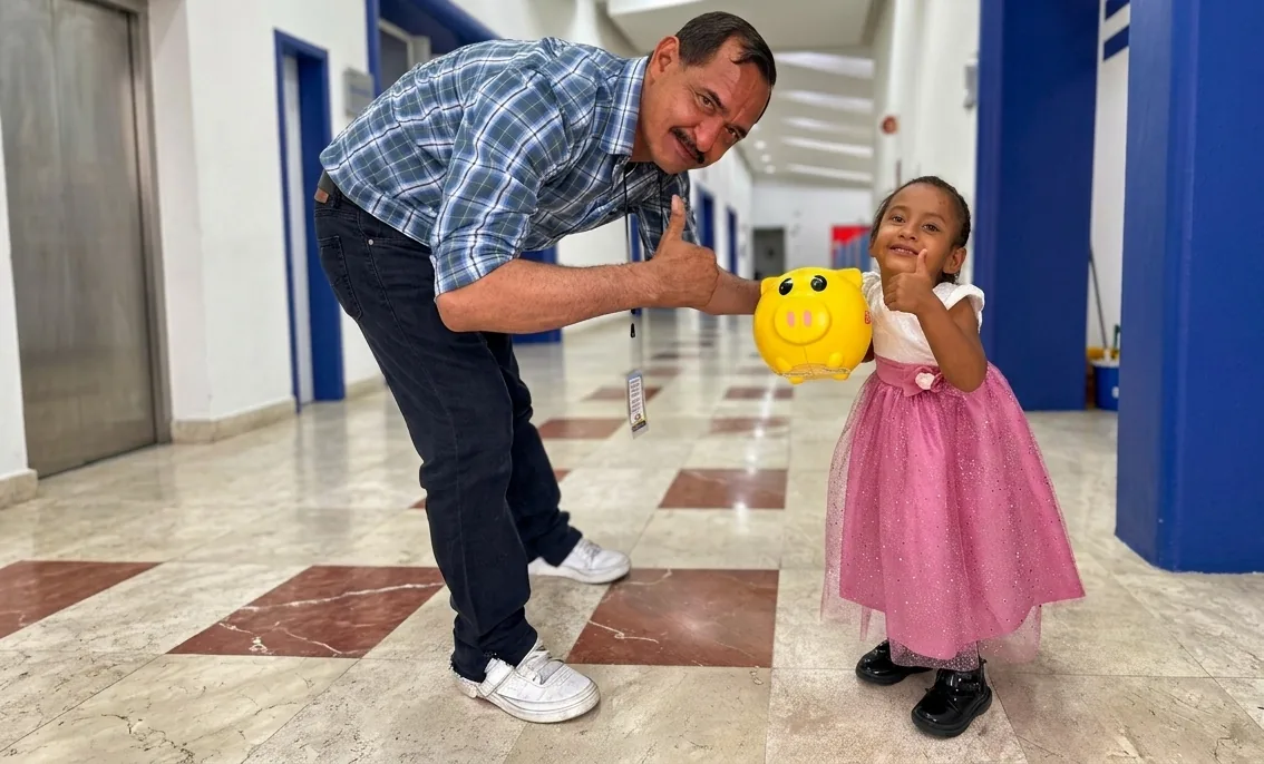 Yurián y su papá sonriendo en un CRIT, sosteniendo una alcancía de donativos